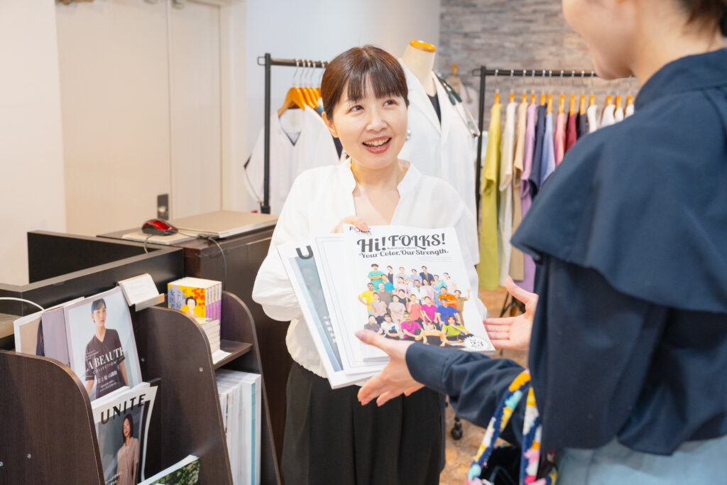 写真：プロフェッサーズラウンド・スタッフが、SORAさんに今回試着サンプルを送るスクラブのカタログを一緒におくりますよと話している様子