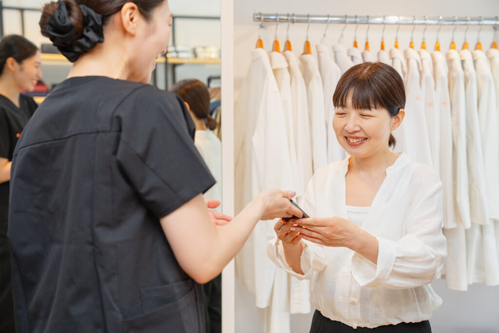 写真：プロフェッサーズラウンド・スタッフに、着用写真をお願いするSORAさん。SORAさんのスマホを受け取るプロフェッサーズラウンド・スタッフ