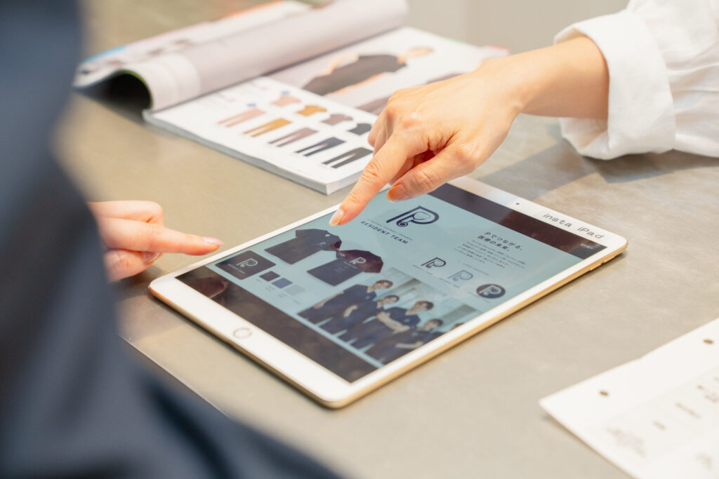 写真：ipadを見ながらロゴ刺繡を購入したスクラブに入れる場所を指定している様子